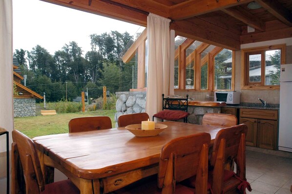A wooden dining table with six chairs, a candle, and a stone wall in the background.
