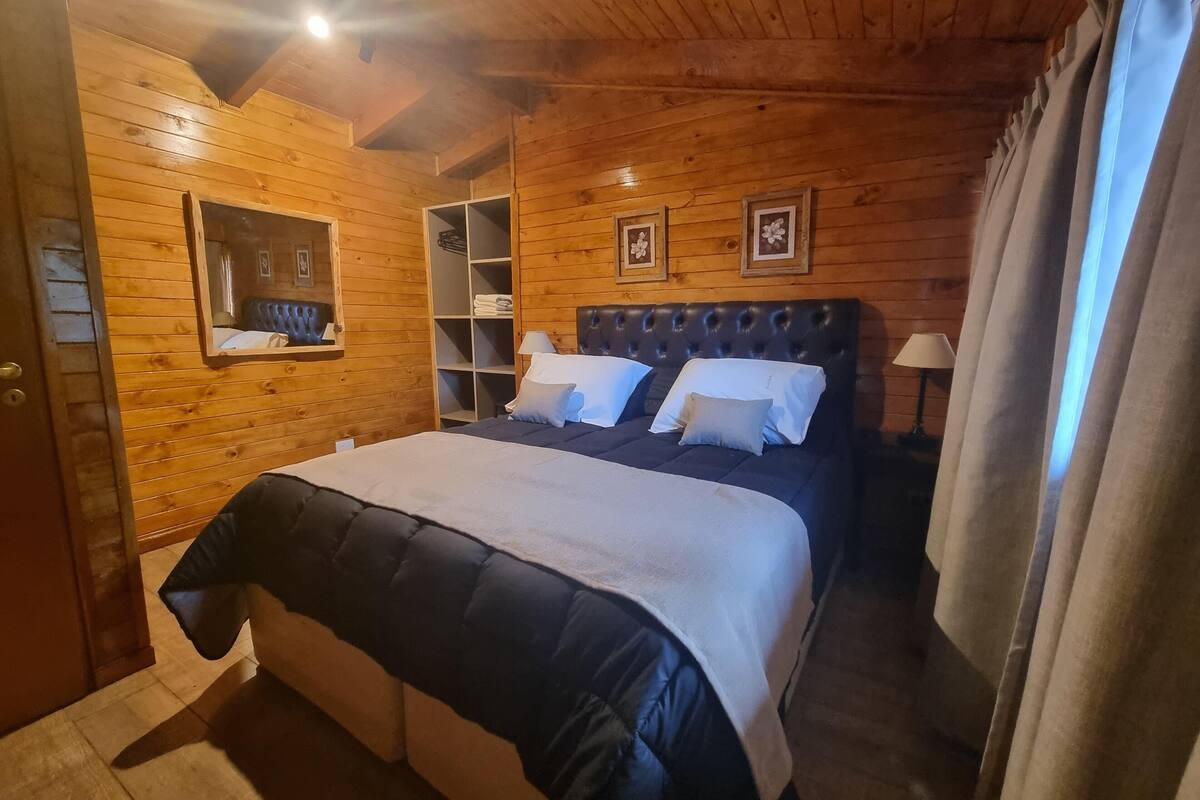 Un dormitorio con paneles de madera, una cama grande, un armario empotrado y una ventana con cortinas.