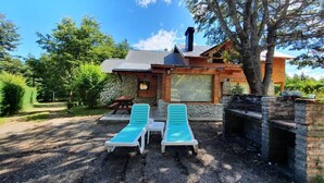 A rustic cabin with a stone exterior, a wooden deck, and two lounge chairs.