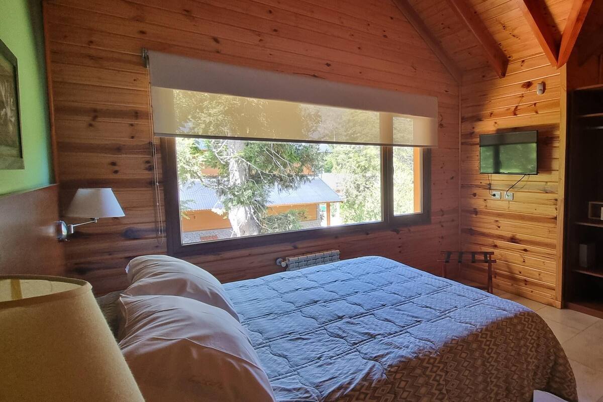 Dormitorio de cabaña de madera con cama, ventana, televisor y armario.