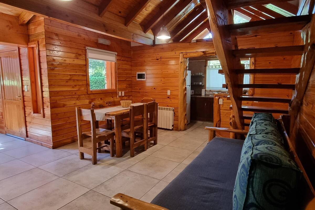 Interior de una cabaña de madera con comedor, sofá y cocina.