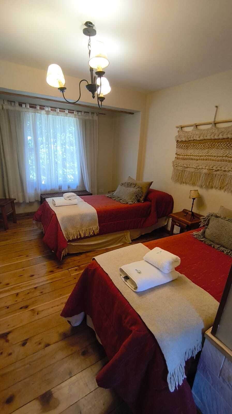 Ein Hotelzimmer mit zwei Betten, Holzboden, einer Chandelierleuchtre und einer Wanddekoration aus Makramee.