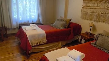 Habitación de hotel con dos camas, suelo de madera, candelabro y un tapiz de macramé en la pared.