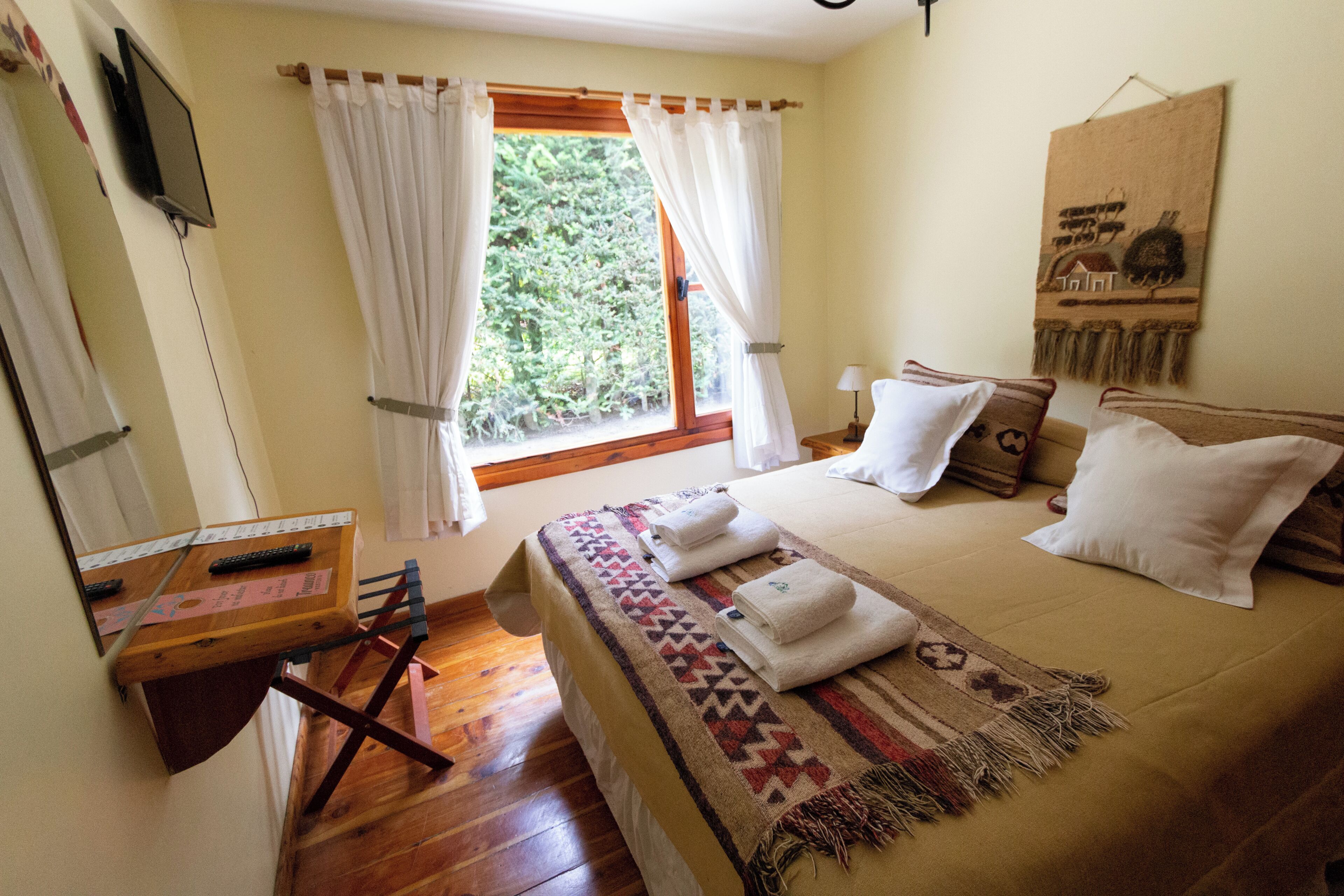 Ein Schlafzimmer mit Bett, Schreibtisch, einem Fenster mit Vorhängen und einem Wandbild.