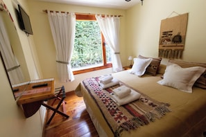 Quarto com cama, escrivaninha, janela com cortinas e uma obra de arte na parede.