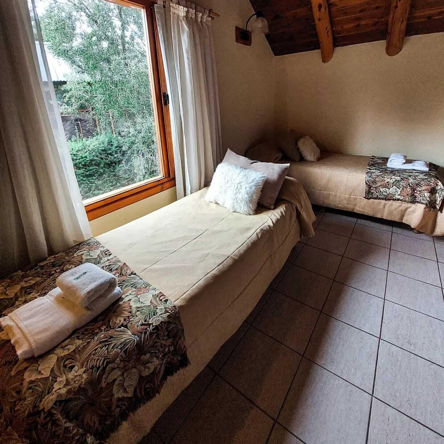 A room with two beds, a window with curtains, and a tiled floor.