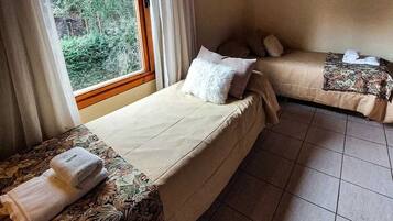A room with two beds, a window with curtains, and a tiled floor.