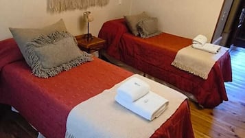 Una habitación con dos camas, piso de madera, un tapiz en la pared, una lámpara de pared y una puerta que da al exterior.