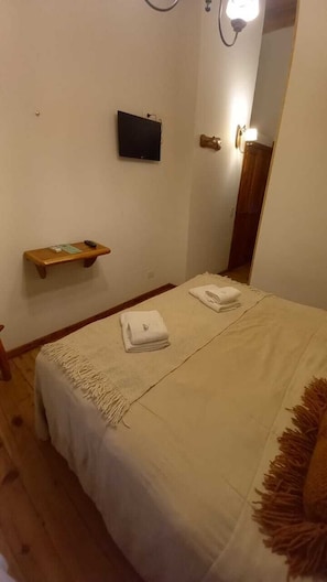 Een slaapkamer met een bed, nachtkastje, een tv aan de muur en een spiegel.