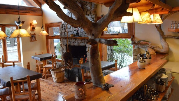Ein rustikales Interieur mit Holzmöbeln, einem Kamin aus Stein und hängenden Lampen.