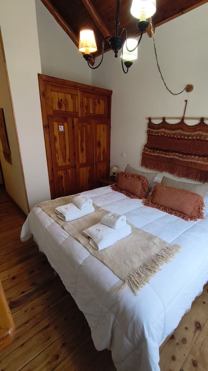 Un dormitorio con piso de madera, una cama con ropa de cama blanca, un armario de madera y un tapiz colgante.