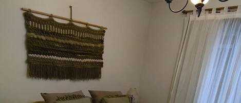 A room with a bed, a bedside table, a hanging tapestry, and a chandelier.