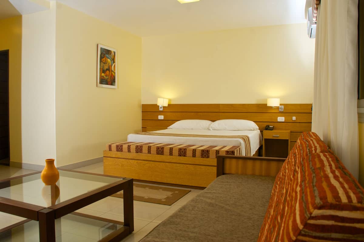 Ein Hotelzimmer mit Bett, Nachttischen, einem Glastisch, einer Couch und einem Bild an der Wand.