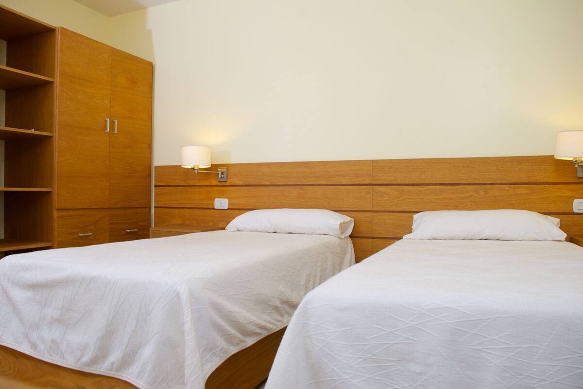 Ein Hotelzimmer mit zwei Einzelbetten, einem Holzschrank und Nachttischlampen.