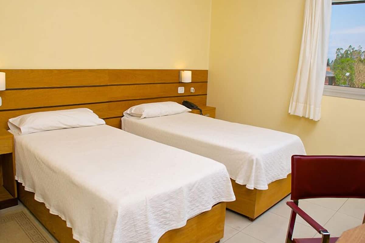 Ein Hotelzimmer mit zwei Einzelbetten, einem hölzernen Kopfteil, Nachttischlampen, einem kleinen Tisch und einem Sessel.