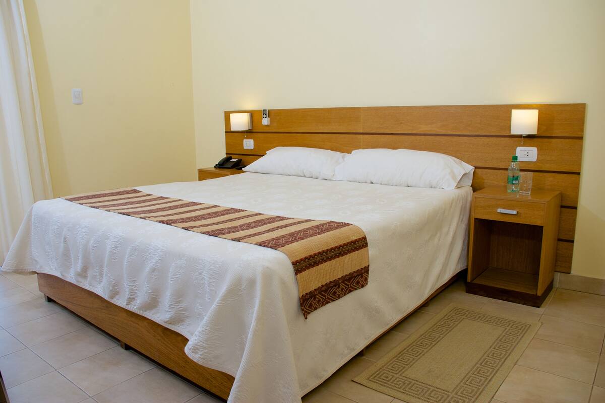 Ein Hotelzimmer mit einem großen Bett, einem Holzkopfteil, Nachttischen und einem Beistelltisch.