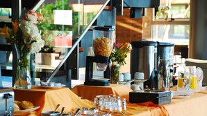 Montaje de desayuno buffet con diversos alimentos, una estación de café y un jarrón con flores.