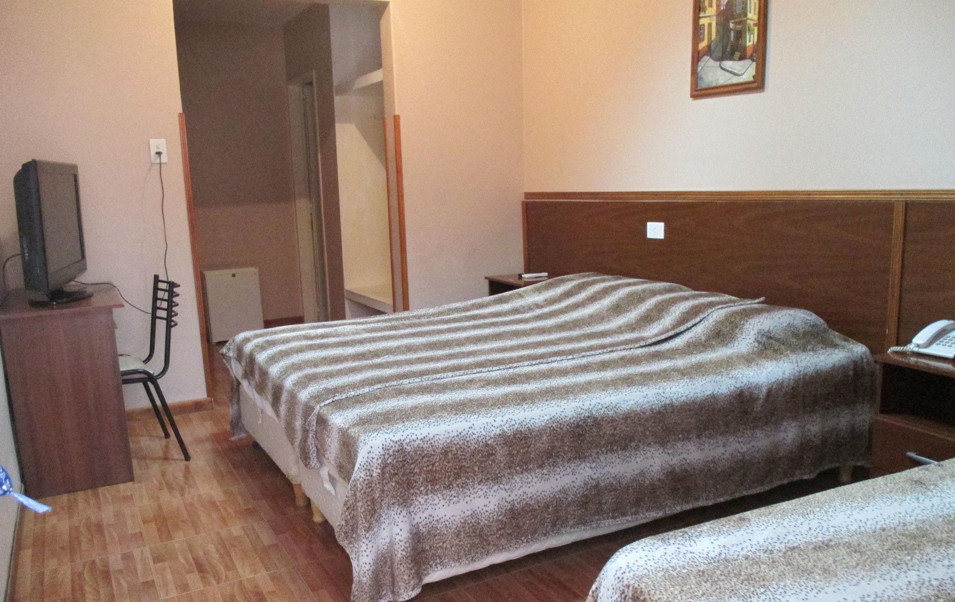 A room with two beds, a television on a stand, a chair, and a painting on the wall.