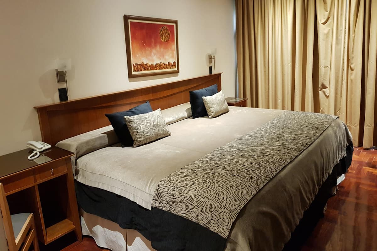 Hotelkamer met een groot bed, nachtkastje met telefoon, schilderij aan de muur en raam met gordijnen.