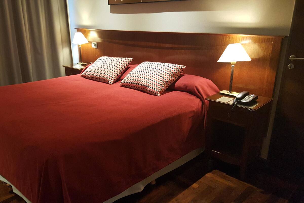 Een hotelkamer met een groot bed, twee bedlampen en een houten hoofdbord.