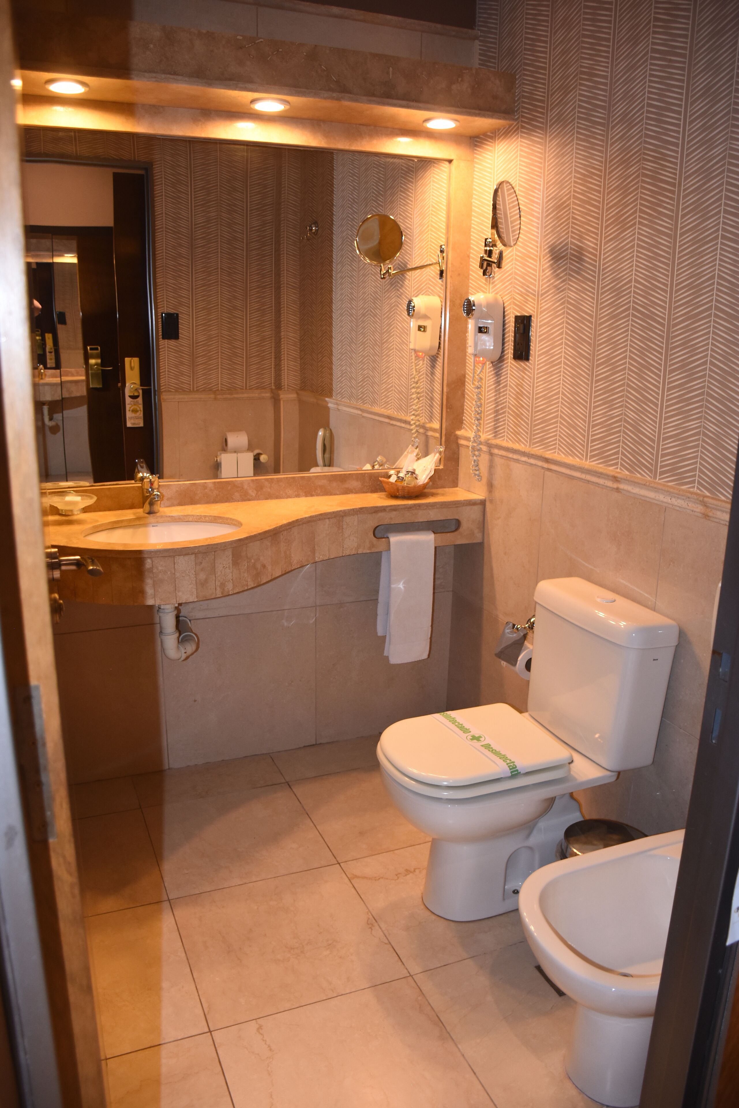 Un baño con lavamanos, espejo, inodoro y toallero.
