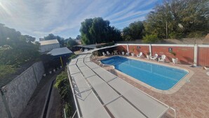 Une piscine dotée de chaises longues et d’un espace abrité, entourée de murs en briques et de verdure.
