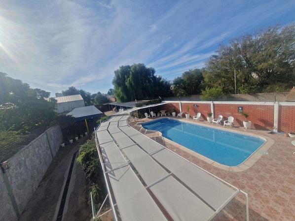 A swimming pool with sun loungers and a covered area, surrounded by brick walls and greenery. - Hotel Pueblo Huarpe (San Luis City)