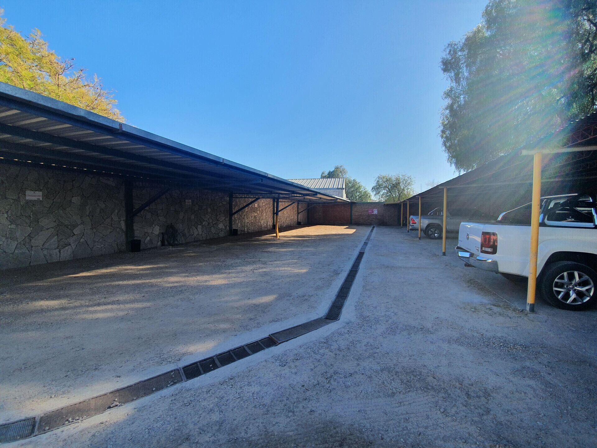 Un espacio al aire libre cubierto con un camino de grava, paredes de piedra y una camioneta blanca estacionada.