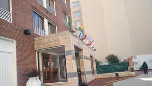 Fachada de hotel em pedra, com várias bandeiras e uma grande planta em vaso.