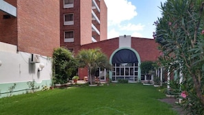Um pátio com gramado, um edifício de tijolos e uma área coberta com uma grande janela.
