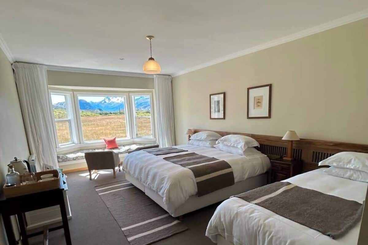 Ein Hotelzimmer mit zwei Betten, einem Schreibtisch, einem Stuhl, einem Fenster mit Ausblick und einer Hängeleuchte.
