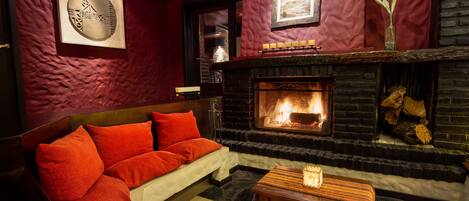 Una habitación acogedora con chimenea, paredes rojas y un sofá con cojines rojos.