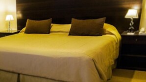 Ein ordentlich bezogenes Bett mit gelber Tagesdecke und zwei Kissen, neben denen Nachttische mit Lampen stehen.