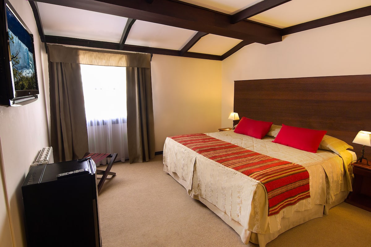 Une chambre d’hôtel avec un lit, un bureau avec un clavier, une chaise et une fenêtre avec des rideaux.
