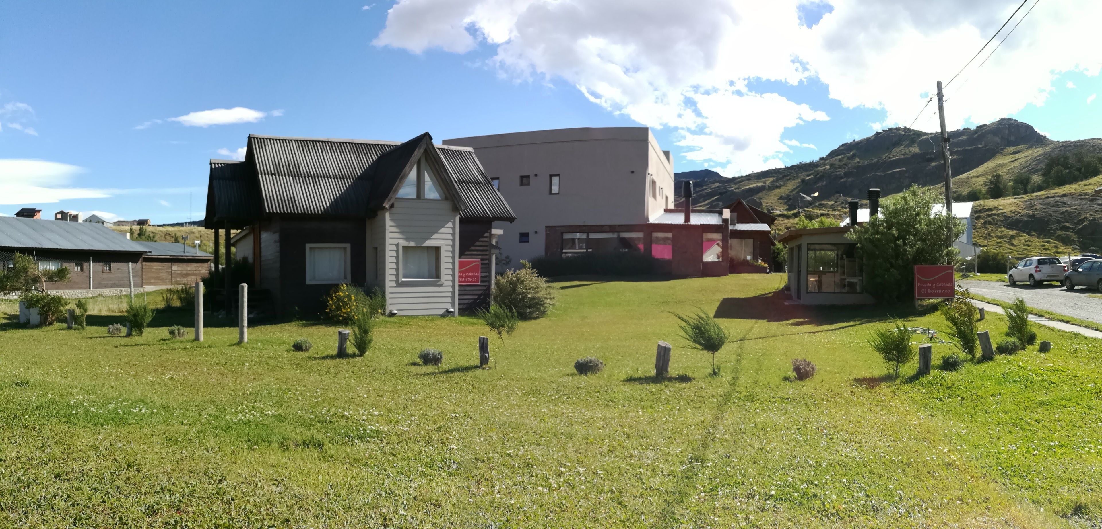 Un bâtiment doté d’un toit en pente et d’une partie de toit plate, entouré d’une pelouse bien entretenue, agrémentée de petits arbustes et de quelques arbres.