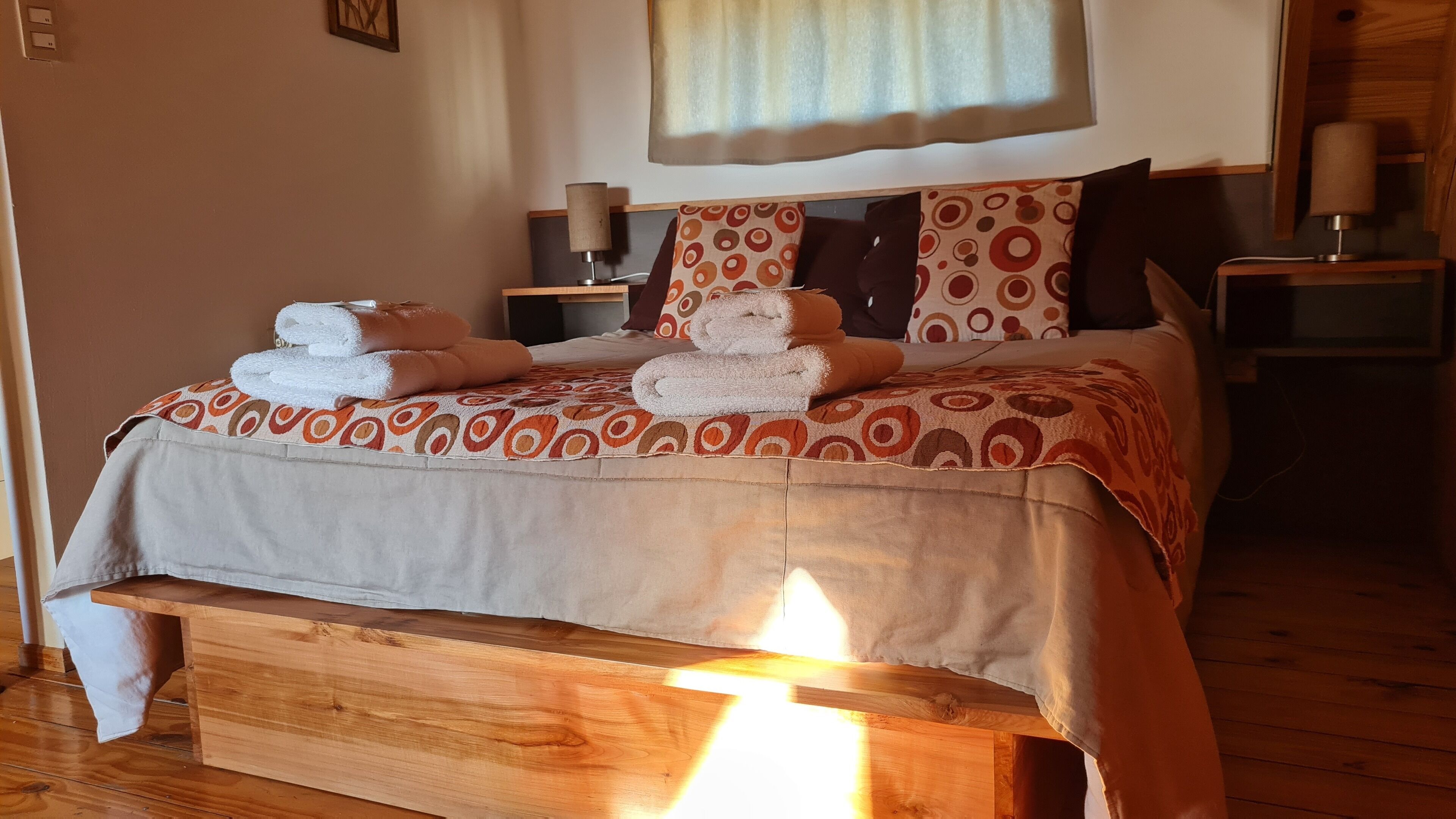 A neatly made bed with towels, a patterned bedspread, and a wooden headboard.