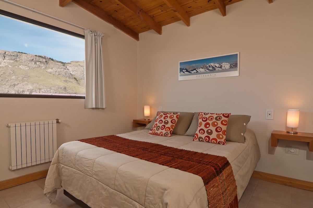 Un dormitorio con cama, ventana con vistas a un paisaje montañoso, radiador y un cuadro enmarcado en la pared.