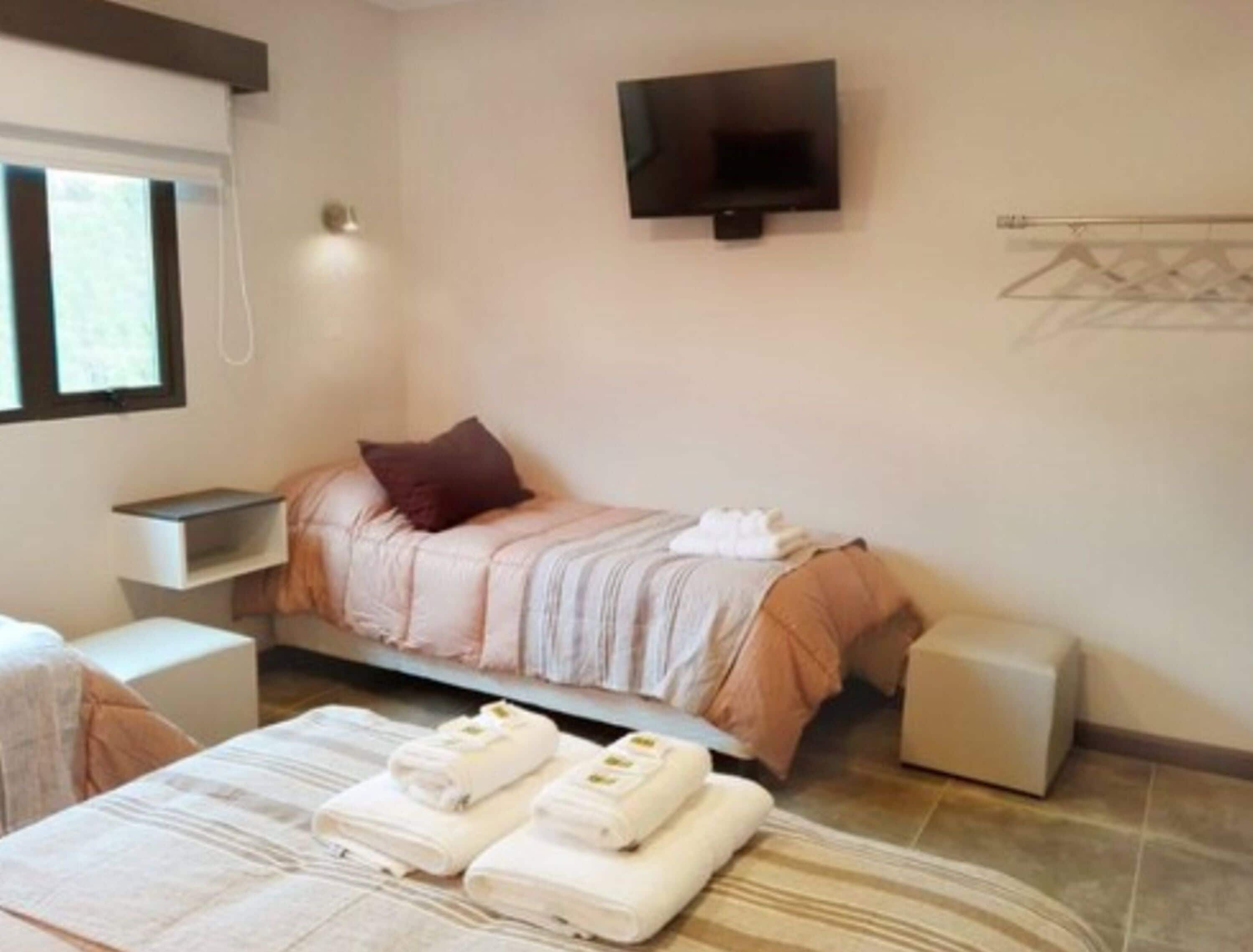 A hotel room with a bed, a TV, a bedside table, a chair, and a small table with towels.
