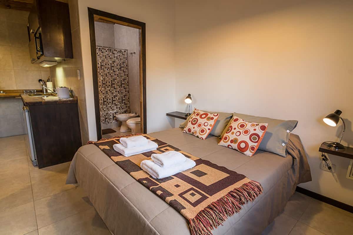 Un dormitorio con cama, dos lámparas de noche, baño y kitchenette.