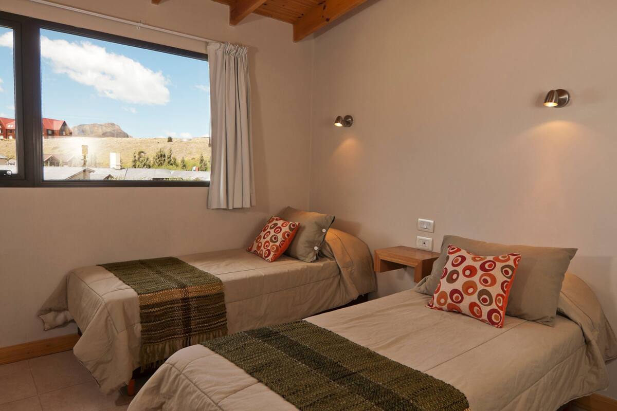 Una habitación con dos camas, una ventana que ofrece vistas a un paisaje y una pequeña mesa con una lámpara.