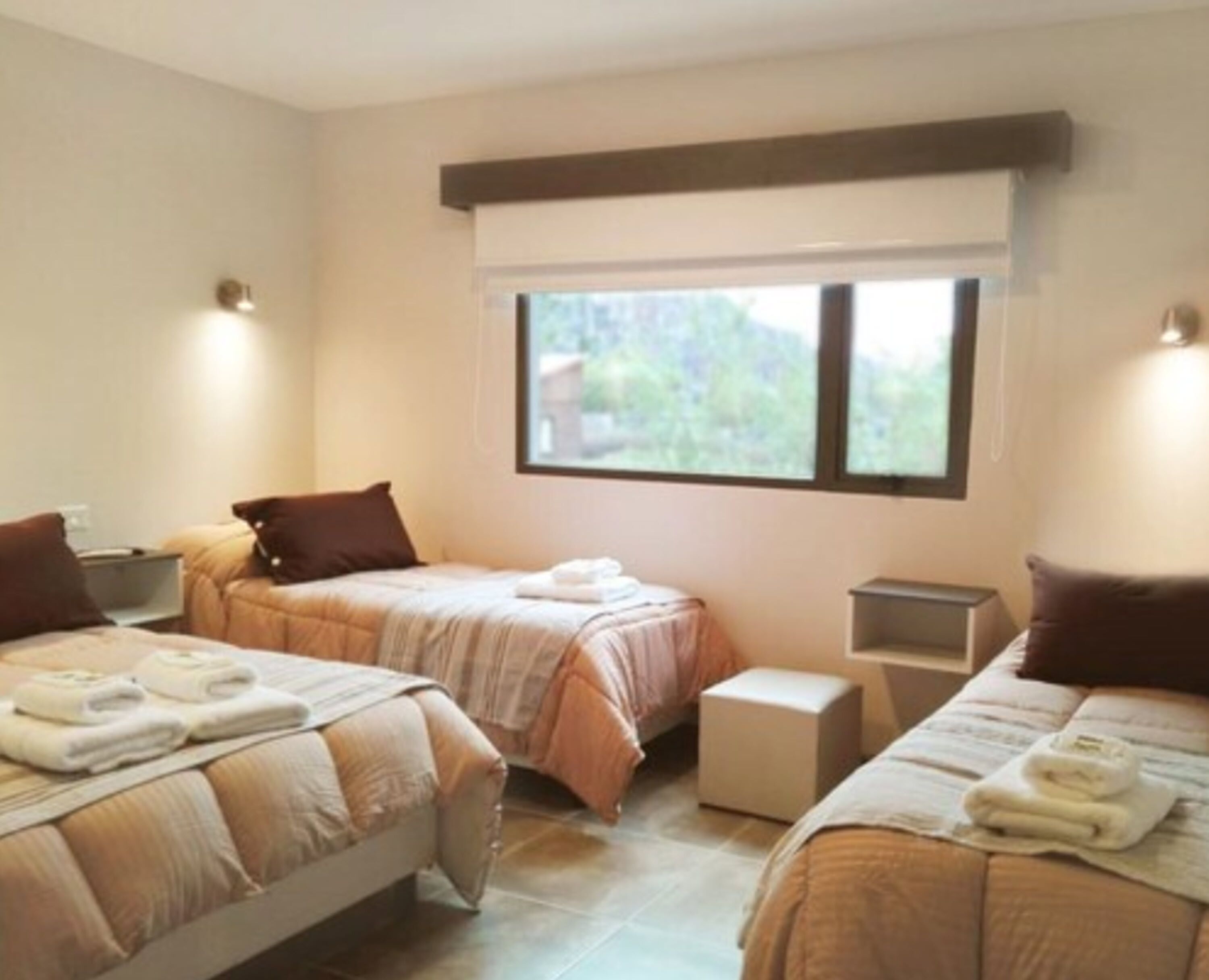 A hotel room with two beds, a window, and a small bedside table.