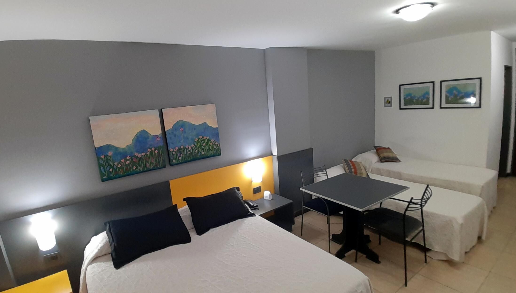 Habitación de hotel con una cama, un escritorio, una silla, una mesa y dos cuadros en la pared.