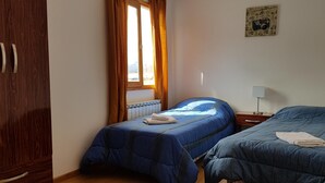 A bedroom with two beds, wooden wardrobe, and a window with curtains. - Los Pinos Apart Hotel (Ushuaia)