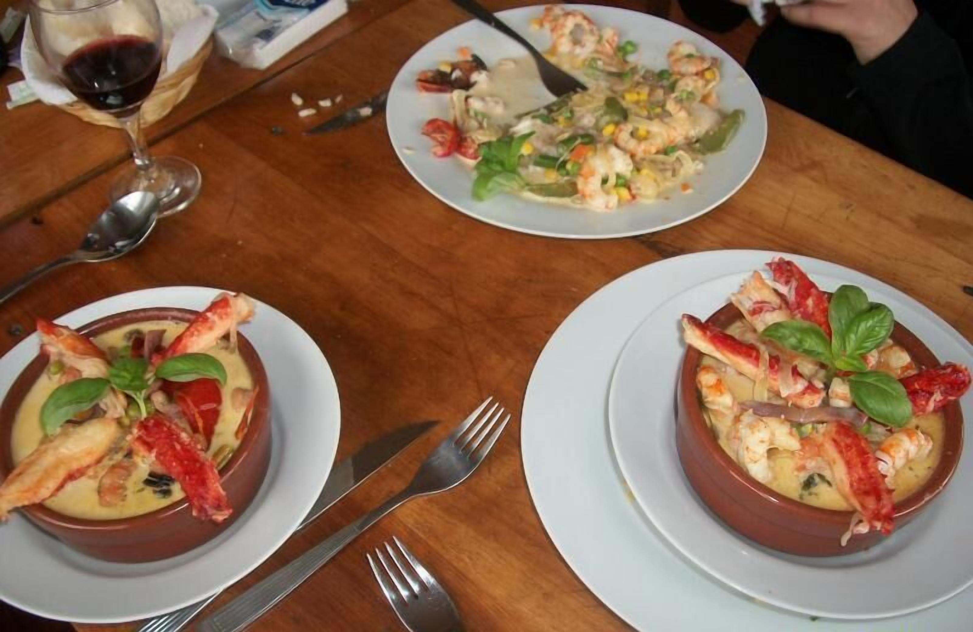 Uma mesa de jantar com três pratos de frutos do mar, uma taça de vinho e talheres.