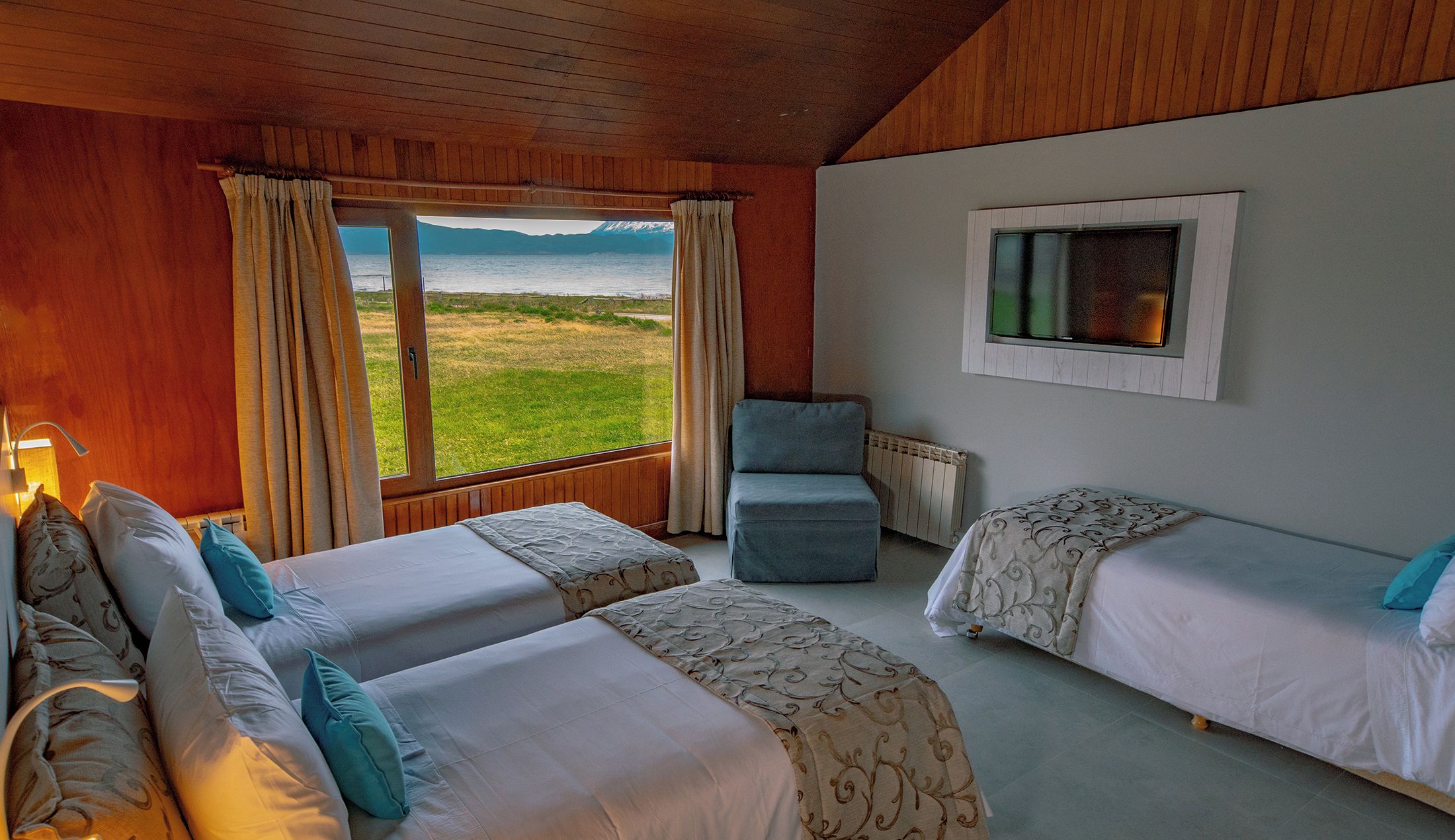 Una habitación con dos camas, una silla y una ventana con vistas a un campo y montañas.