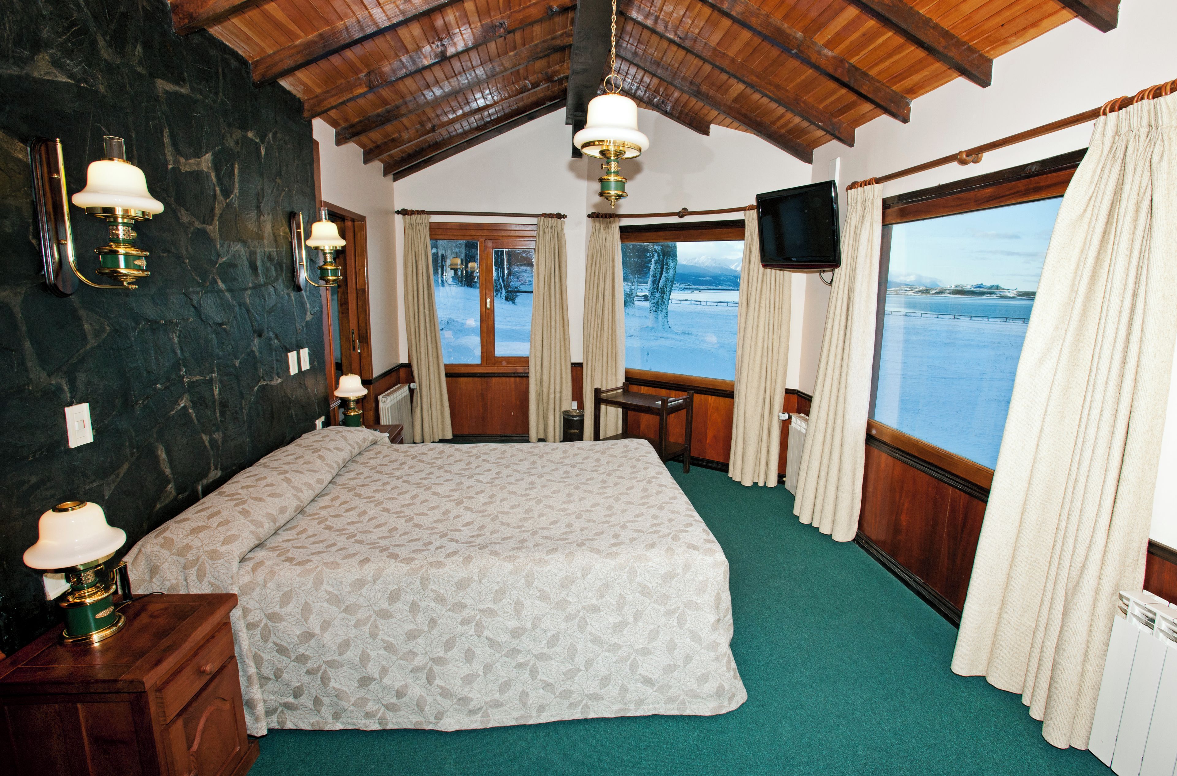 A room with a large bed, a desk, a chair, a television, and a view of a snowy landscape.