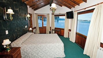A room with a large bed, a desk, a chair, a television, and a view of a snowy landscape.
