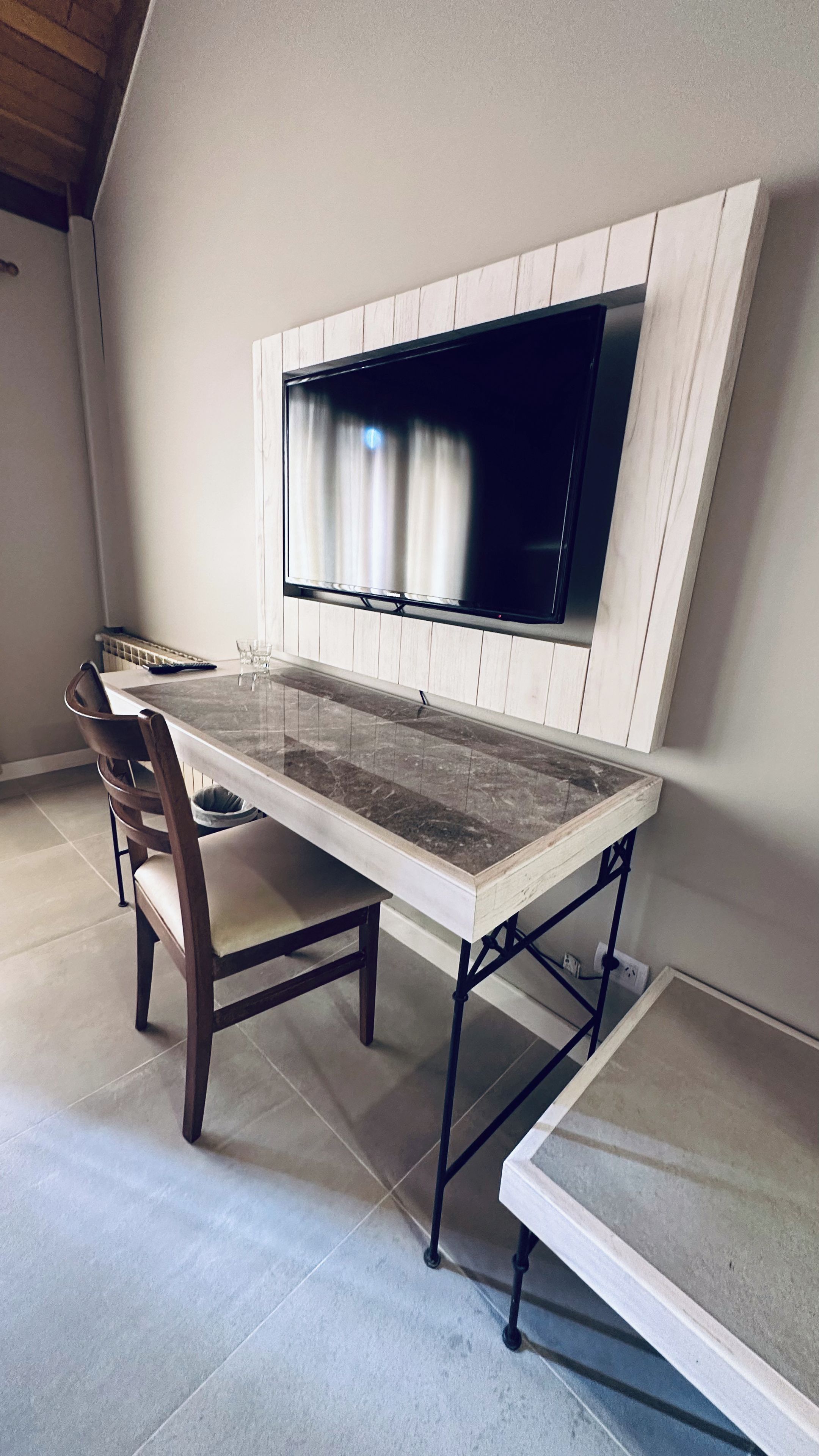 Una zona de menjador amb una taula de marbre, cadires de fusta i un televisor fixat a una paret blanca.