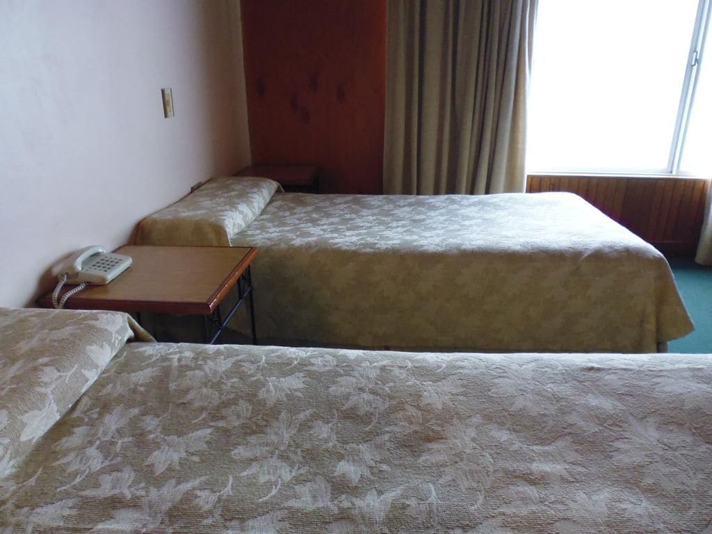 Habitación de hotel con dos camas, teléfono en la mesita de noche y ventana con cortinas.