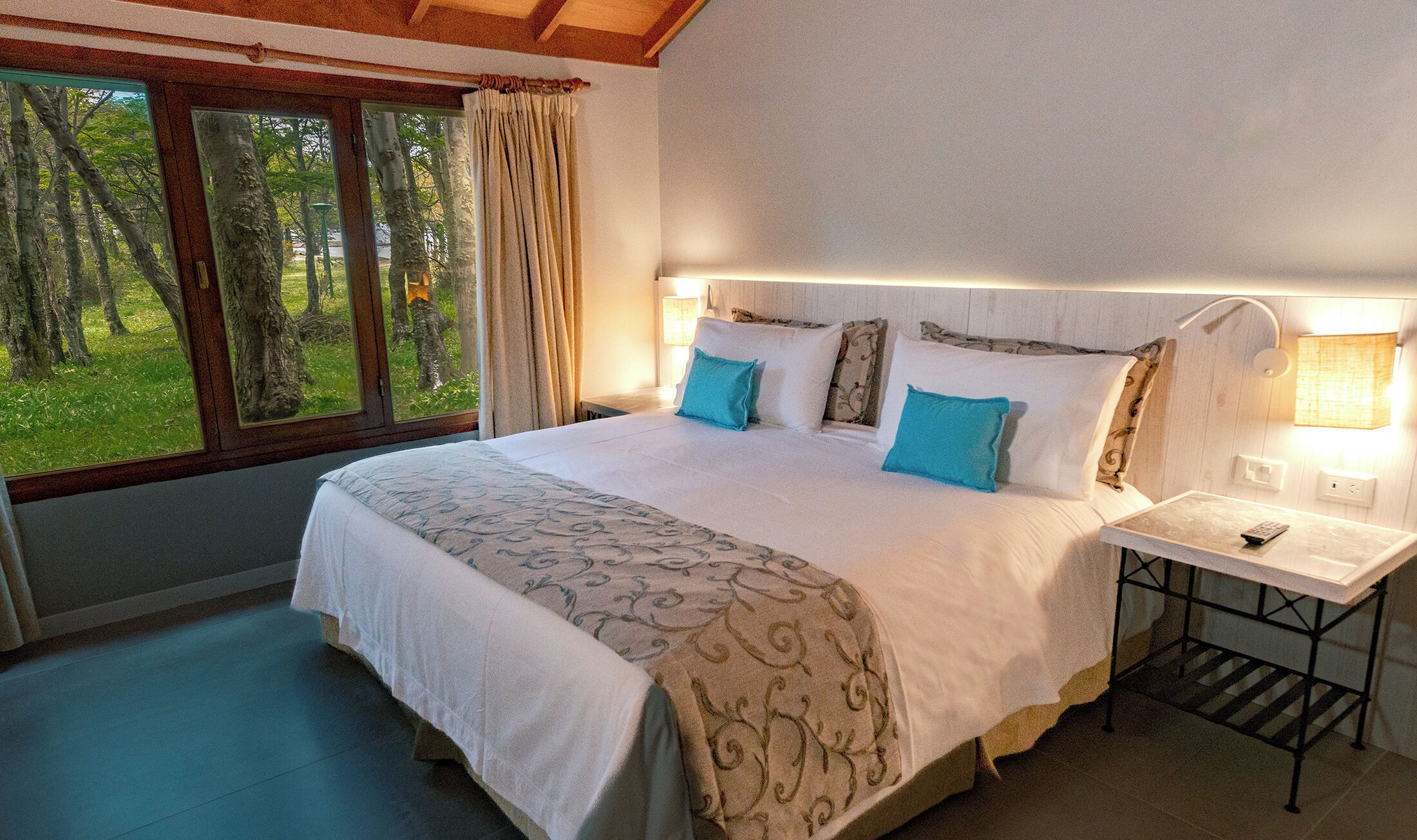 A bedroom with a large bed, two bedside lamps, a nightstand, and a window with curtains.
